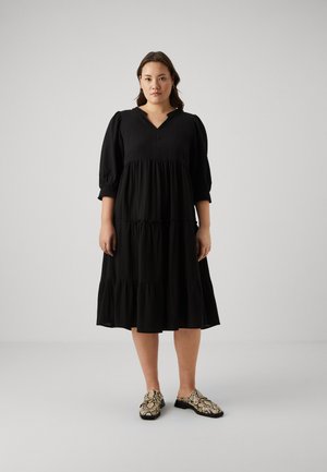 Black tiered dress with puff sleeves and a V-neckline, paired with patterned slip-on shoes featuring a snake print design.
