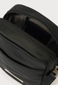 Fekete nejlon táska cipzáras zárral és ezüstszínű fém alkatrészekkel. Texturált felülettel és belső zsebbel rendelkezik. Állítható pánt.