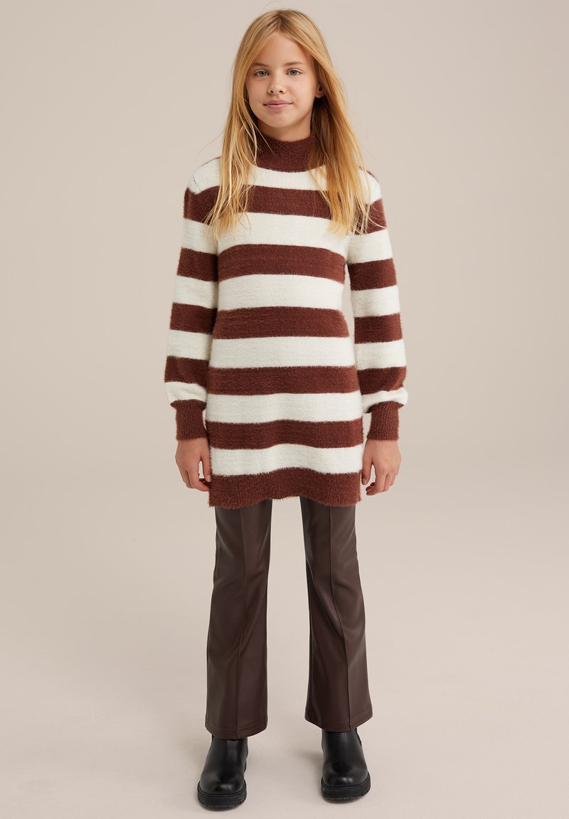 Hnedo-krémový pruhovaný sveter s dlhým rukávom a vysokým golierom. Spárované s hnedými topánkami z umelého koženého materiálu s širokými nohavicami a čiernymi členkovými čižmami.