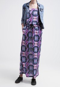 Robe maxi en tissu à motifs avec des nuances de bleu, rose et noir ; associée à une veste en jean. Accentuée d'une taille à cordon et de poches.