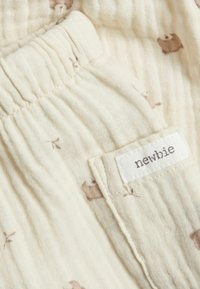 Helle Baumwollstoffe mit einer weichen, strukturierten Oberfläche und braunem Tierdruck. Elastischer Bund mit einem kleinen angenähten Etikett, auf dem "newbie" steht.