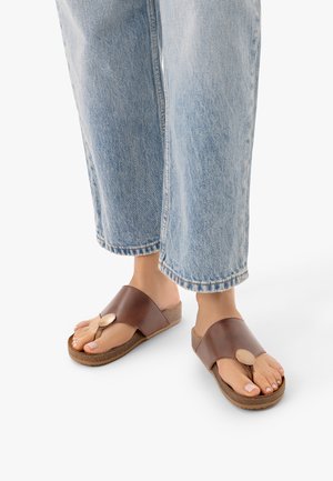 Pieds portant des sandales en cuir marron à enfiler avec une large bride et un jean denim bleu clair raccourci.