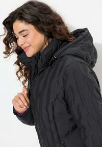 Svart pufferjacka med en texturerad yta, som har huva, hög krage och dragkedjestängning. Insidan visar en färgklick av lila.