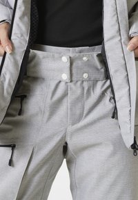 Šedé lyžařské kalhoty vyrobené z texturované látky, s dvojitým knoflíkovým zapínáním, dvěma bočními kapsami a nastavitelnými манžetami se zipy.