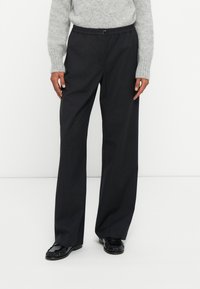 Donkergrijze, wijde broek met een elastische taille en knoopsluiting. Soepele stof met een subtiele glans, gecombineerd met glanzende zwarte schoenen.