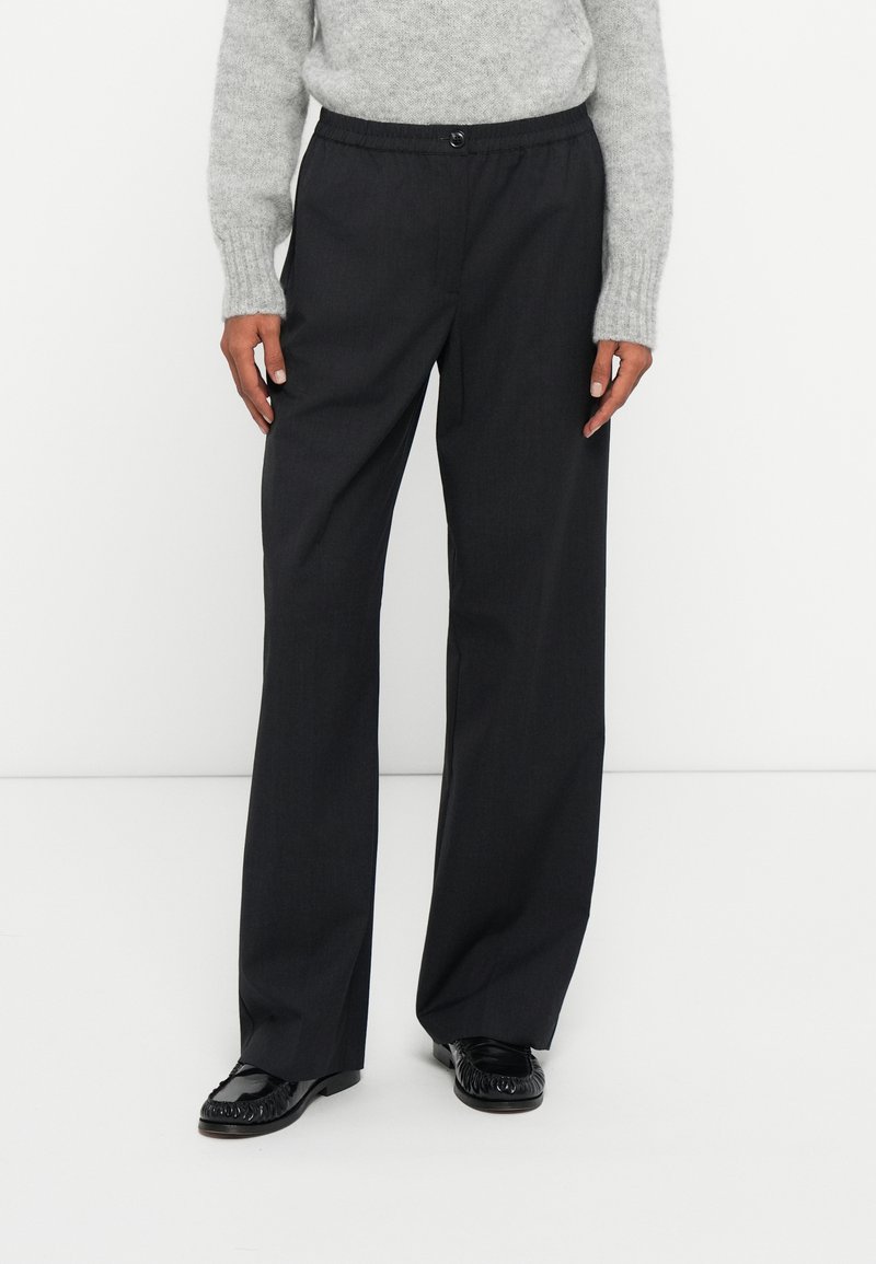 Donkergrijze, wijde broek met een elastische taille en knoopsluiting. Soepele stof met een subtiele glans, gecombineerd met glanzende zwarte schoenen.