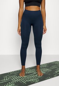 Leggings blu navy a vita alta con pannelli testurizzati, design aderente e tessuto morbido, indossati con un crop top nero, su un tappetino da yoga con motivi.