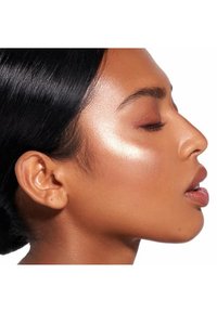 Vista de perfil de un modelo con piel suave de tono marrón medio, pómulos destacados y cabello negro liso, presentando un maquillaje sutil y un tono de labios natural.