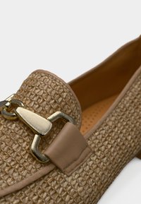 Μπεζ πλεκτά μοκασίνια με υφή στην επιφάνεια, μεταλλική αλυσίδα ως διακόσμηση και λείες δερμάτινες λεπτομέρειες. Στρογγυλεμένο σχήμα και επίπεδη σόλα.