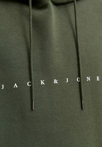 Grüne Kapuzenjacke mit Kordeln und metallischen Spitzen. Mit weißem Aufdruck "JACK & JONES" auf der Vorderseite. Weicher Stoff mit einer glatten Textur.