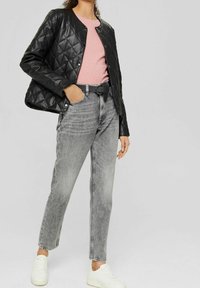 Giacca nera trapuntata sopra un maglione rosa a coste, abbinata a jeans grigi a vita alta e sneaker bianche. Presenta un collo rotondo e chiusure a scatto.