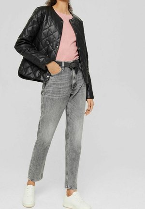Giacca nera trapuntata sopra un maglione rosa a coste, abbinata a jeans grigi a vita alta e sneaker bianche. Presenta un collo rotondo e chiusure a scatto.