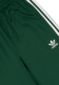 Gröna träningsbyxor gjorda av slätt tyg, med vita sidosträck och en broderad vit Adidas-logga på benet.
