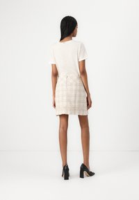 T-shirt a righe color crema, maniche corte. Mini gonna in tweed beige chiaro con una trama testurizzata. Scarpe nere con tacco alto e spesso.