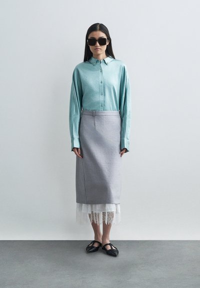 Απαλή μπλε πουκάμισο με μακρύ μανίκι, συνδυασμένο με μια γκρίζα μολυβένια φούστα και μια λευκή δαντελένια φούστα από κάτω. Μαύρα, υφασμένα παπούτσια.