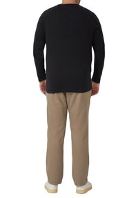 Zwart shirt met lange mouwen en raglanmouwen, gecombineerd met lichtbruine broek en witte sneakers. Eenvoudig ontwerp en comfortabele pasvorm.