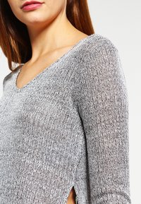 Maglione grigio a coste con scollo a V, maniche lunghe e spacchi laterali, realizzato in un tessuto morbido e testurizzato.