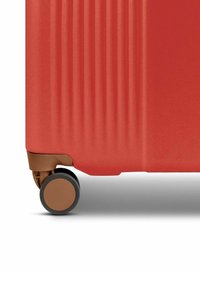 Red luggage with a textured surface featuring vertical ridges, equipped with a brown wheel. The design emphasizes a sleek, modern shape.