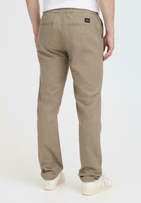 Pantalones beige texturizados con cintura elástica y dos bolsillos traseros, combinados con zapatillas blancas.