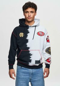 Kapuzensweatshirt mit einem geteilten Design, schwarz auf der einen Seite und weiß auf der anderen, mit roten Akzenten und San Francisco 49ers Logos.