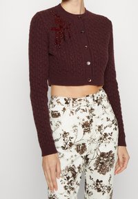 Burgunderfarbene, aus Kabelstrick gefertigte kurze Strickjacke mit sechs Knopfverschlüssen und bestickter Blumendekoration auf der linken Schulter.