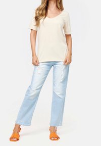 Beige top s krátkým rukávem a výstřihem do V v kombinaci se světle modrými roztrhanými širokými džíny a oranžovými sandály s fringingem.