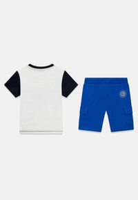 T-shirt bianca con maniche corte blu scuro e scollatura rotonda, abbinata a pantaloni cargo blu con tasche laterali e dettagli con logo.