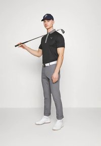 Golfa apģērbs, kas sastāv no melnā polo krekla ar pelēku apkakli, pelēkām biksēm, baltas jostas un baltām sporta kedām, kā arī golfa nūja un tumši zils cepure.