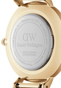 Zelta tonī tērauda pulksteņa aizmugurē ir iegravēts "DW" logo, modeļa informācija un ūdensizturības detaļas ap sudraba centru.