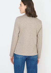 Beige visgraat blazer met lange mouwen en een getailleerde pasvorm, gecombineerd met blauwe denim jeans. De stof heeft een gestructureerde, geweven uitstraling.
