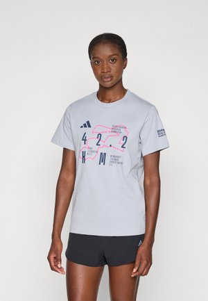Kvinde iført en lys grå T-shirt med lyserød og navy 42,2 KM maratonrute grafik og sorte shorts mod en ensfarvet baggrund.