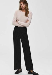 Lichtroze lange mouw trui gecombineerd met hoge taille zwarte brede broek. Zwarte loafers maken de outfit compleet. Gladde stoftextuur.