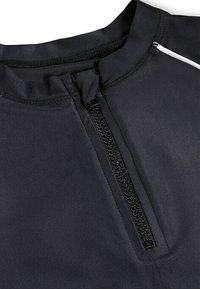 Top atletico nero con zip frontale a metà, caratterizzato da un tessuto morbido, un colletto alto e una striscia bianca a contrasto lungo la cucitura della spalla.