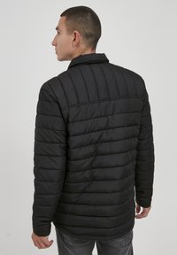 Sort dunjakke med quiltet mønster. Har en stålkrave og et let materiale, designet til varme og komfort i koldt vejr.