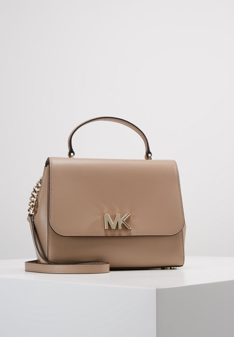 Sac à main structuré beige avec logo MK doré, anse supérieure, bandoulière ornée de chaîne, exposé sur une surface blanche devant un fond uni.