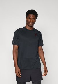 Czarny, krótki rękawek koszulka sportowa z teksturowanym wzorem, z różowym logo Nike na klatce piersiowej i gładkim wykończeniem materiału.