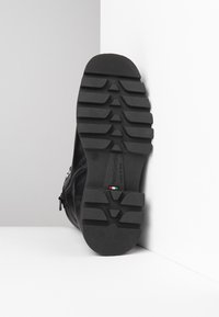 Black leather boot sole with deep grooves for traction, featuring a smooth texture and embossed brand logo. Designed for durability and grip.