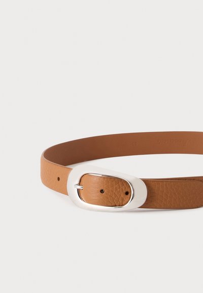 Ceinture en cuir marron texturé avec grande boucle ovale argentée et deux trous de réglage sur fond blanc.