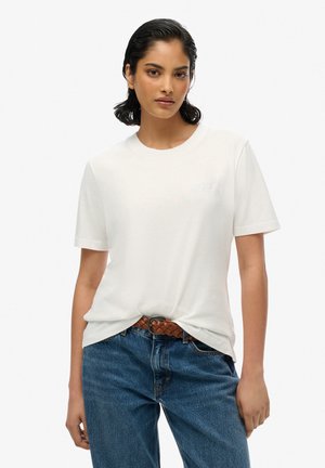 Biała bawełniana koszulka z okrągłym dekoltem i krótkimi rękawami, z delikatnie haftowanym logo na piersi, w połączeniu z niebieskimi dżinsowymi spodniami.