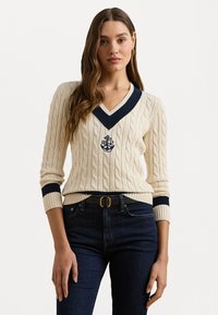 Κρέμα πλεκτό πουλόβερ με ναυτικό V-ντεκολτέ και μανίκια. Διαθέτει κεντητό έμβλημα άγκυρας. Φοριέται με σκούρες τζιν παντελόνες και μαύρη ζώνη.