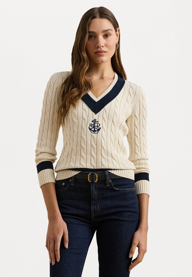 Κρέμα πλεκτό πουλόβερ με ναυτικό V-ντεκολτέ και μανίκια. Διαθέτει κεντητό έμβλημα άγκυρας. Φοριέται με σκούρες τζιν παντελόνες και μαύρη ζώνη.