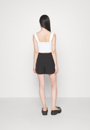 Haut court blanc texturé avec des bretelles volantées, associé à un short noir taille haute, vu de dos. Des chaussures à plateforme noires complètent la tenue.