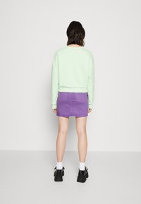 Felpa verde menta, gonna di jeans viola e scarpe con plateau nere con calzini bianchi; cuciture visibili sulla gonna e vestibilità rilassata della felpa.