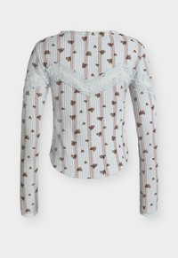 Bijela majica s dugim rukavima, izrađena od waffle tkanine, s malim smeđim cvjetnim uzorkom, okomitim bež prugama i čipkastim obrubom na leđima i rukavima.