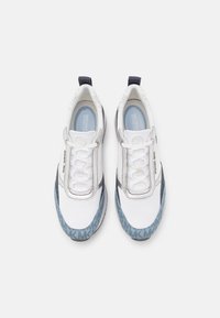 White sneakers with blue accent detailing, textured fabric, lace-up closure, and logo on the side. Features a cushioned insole and rubber sole.