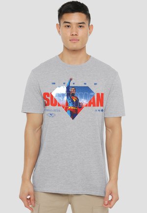 Young man wearing a grey T-shirt featuring Superman flying upward with text "Look up in the sky" and "Superman" in red and blue.