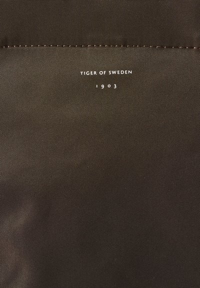 Rudas medžiaga su tvarkingais siuvinėjimais ir balta tekstu, skaitančiu "TIGER OF SWEDEN 1903", sutelkta arti viršaus.
