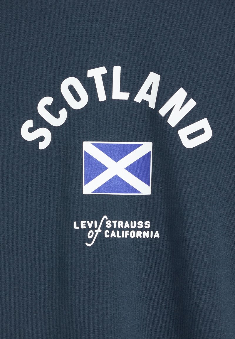 Navy fabric with white text "SCOTLAND" above a blue and white Saltire flag and "Levi Strauss of California" logo below.