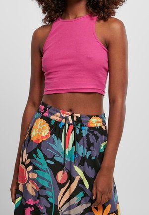 Femme portant un crop top rose sans manches et une jupe noire taille haute avec des motifs floraux colorés sur un fond clair.