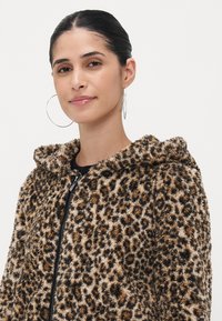 Løveprintet zip-up hettejakke laget av myk kunstpels, med snorhette, teksturert stoff og svart glidelås.